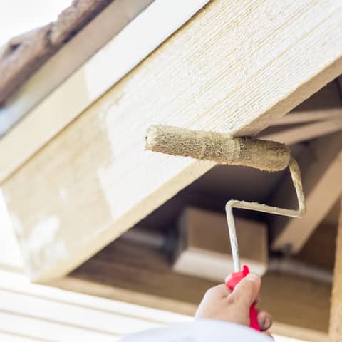 Painter rolling fresh paint onto the underside of an exterior roof overhang and siding