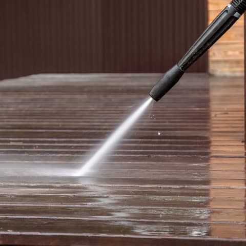 Pressure washer stripping dirt from weathered timber decking, leaving a clean stripe behind