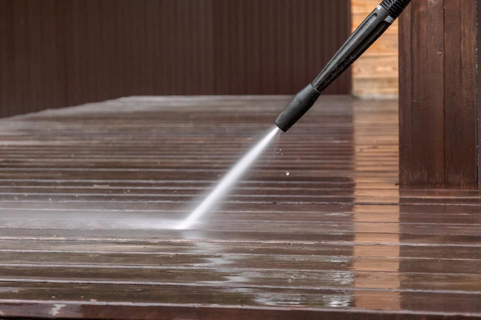 Pressure washer stripping dirt from weathered timber decking, leaving a clean stripe behind