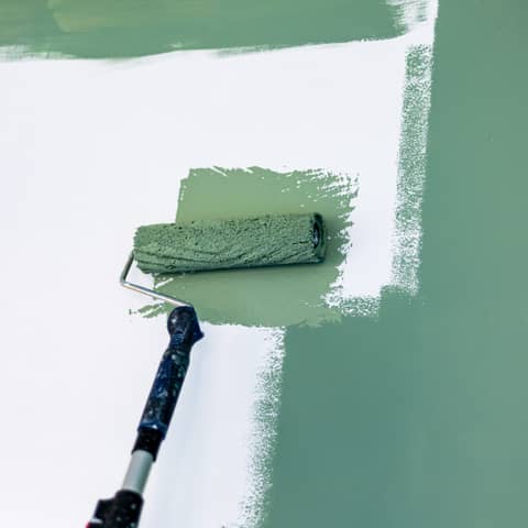 Paint roller applying a fresh coat of soft green paint to an interior wall
