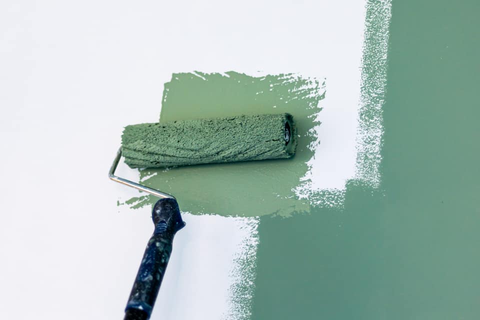 Paint roller applying a fresh coat of soft green paint to an interior wall