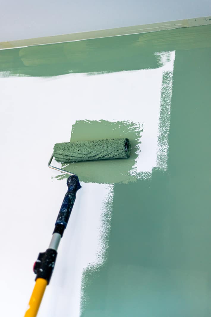 Paint roller applying a fresh coat of soft green paint to an interior wall