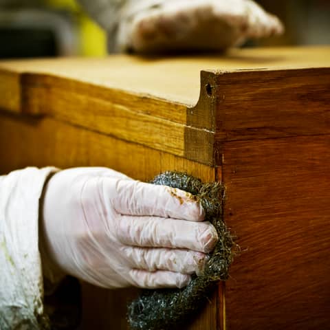 Gloved hand sanding and scouring a wooden surface back to bare timber before finishing